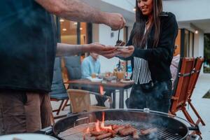 A group of friends and family barbecue together in the evening on the terrace in front of a large modern house photo