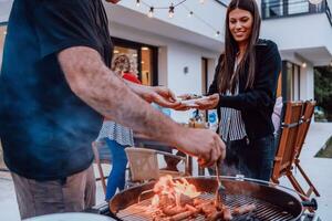 A group of friends and family barbecue together in the evening on the terrace in front of a large modern house photo