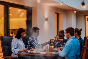 A group of young diverse people having dinner on the terrace of a modern house in the evening. Fun for friends and family. Celebration of holidays, weddings with barbecue. photo