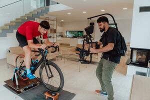 un camarógrafo rodaje un atleta montando un triatlón bicicleta en un simulación máquina en un moderno vivo habitación. formación en pandemia condiciones. foto