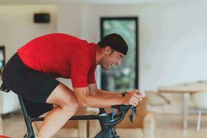 un hombre montando un triatlón bicicleta en un máquina simulación en un moderno vivo habitación. formación durante pandemia condiciones. foto