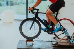 un hombre montando un triatlón bicicleta en un máquina simulación en un moderno vivo habitación. formación durante pandemia condiciones. foto