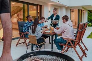 A group of young diverse people having dinner on the terrace of a modern house in the evening. Fun for friends and family. Celebration of holidays, weddings with barbecue. photo