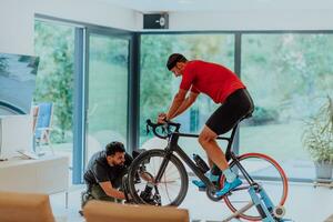un camarógrafo rodaje un atleta montando un triatlón bicicleta en un simulación máquina en un moderno vivo habitación. formación en pandemia condiciones. foto