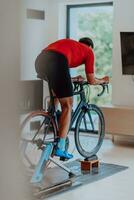 A man riding a triathlon bike on a machine simulation in a modern living room. Training during pandemic conditions. photo