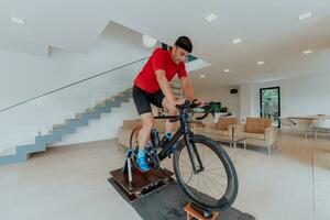 un hombre montando un triatlón bicicleta en un máquina simulación en un moderno vivo habitación. formación durante pandemia condiciones. foto