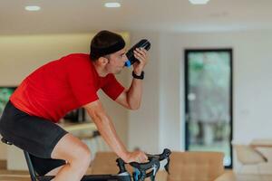 un hombre montando un triatlón bicicleta en un máquina simulación en un moderno vivo habitación. formación durante pandemia condiciones. foto