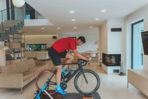 un hombre montando un triatlón bicicleta en un máquina simulación en un moderno vivo habitación. formación durante pandemia condiciones. foto