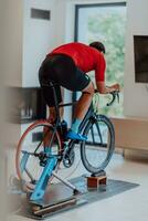 un hombre montando un triatlón bicicleta en un máquina simulación en un moderno vivo habitación. formación durante pandemia condiciones. foto