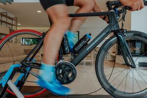 un hombre montando un triatlón bicicleta en un máquina simulación en un moderno vivo habitación. formación durante pandemia condiciones. foto