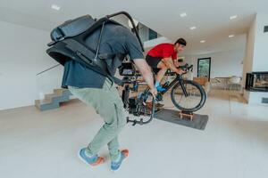 un camarógrafo rodaje un atleta montando un triatlón bicicleta en un simulación máquina en un moderno vivo habitación. formación en pandemia condiciones. foto