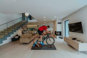 A man riding a triathlon bike on a machine simulation in a modern living room. Training during pandemic conditions. photo