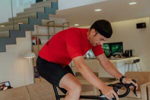 un hombre montando un triatlón bicicleta en un máquina simulación en un moderno vivo habitación. formación durante pandemia condiciones. foto