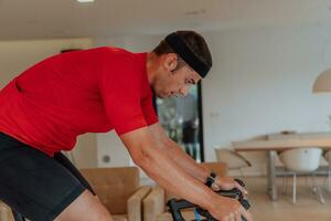 un hombre montando un triatlón bicicleta en un máquina simulación en un moderno vivo habitación. formación durante pandemia condiciones. foto