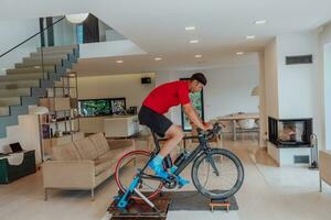 A man riding a triathlon bike on a machine simulation in a modern living room. Training during pandemic conditions. photo