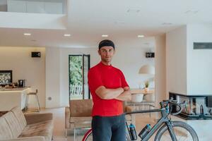 Photo of a determined triathlete standing in a modern large living room, behind him is his training bike