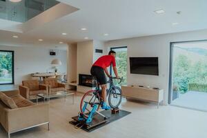 un hombre montando un triatlón bicicleta en un máquina simulación en un moderno vivo habitación. formación durante pandemia condiciones. foto