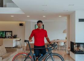 Photo of a determined triathlete standing in a modern large living room, behind him is his training bike