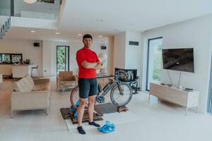Photo of a determined triathlete standing in a modern large living room, behind him is his training bike
