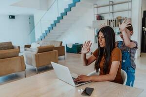 Mother with her daughter talking on laptop with family and friends while sitting in modern living room of big house photo