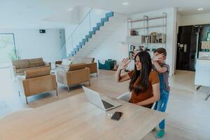 Mother with her daughter talking on laptop with family and friends while sitting in modern living room of big house photo