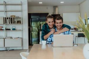 A young married couple is talking to parents, family and friends on a video call via a laptop while sitting in the living room of their modern house photo