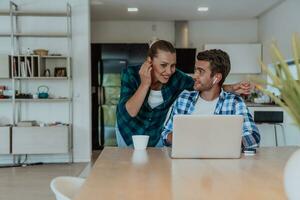 A young married couple is talking to parents, family and friends on a video call via a laptop while sitting in the living room of their modern house photo