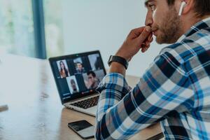 The man sitting at a table in a modern living room, with headphones using a laptop for business video chat, conversation with friends and entertainment photo