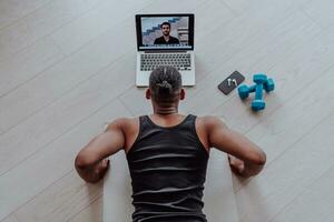 Training At Home. Sporty man doing training while watching online tutorial on laptop, exercising in living room, free space photo