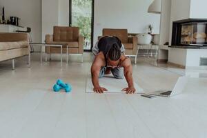 Training At Home. Sporty man doing training while watching online tutorial on laptop, exercising in living room, free space photo