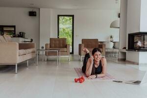 Young woman resting after online training while lying on the living room floor photo