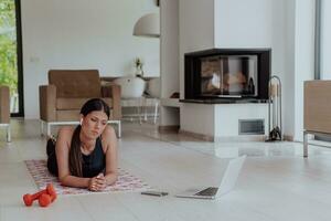 Young woman resting after online training while lying on the living room floor photo