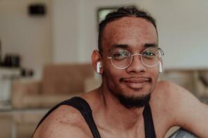 cabeza Disparo de africano americano hombre vistiendo lentes y auriculares sentado en vivo habitación piso foto