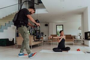 detrás el escena. foto de un camarógrafo grabación un mujer haciendo yoga ejercicios a un en línea formación mientras utilizando y acecho un ordenador portátil