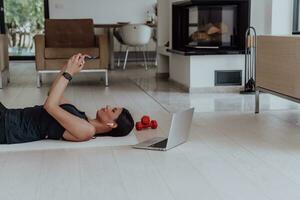 Sportswoman using a smartphone while resting and lying on floor of modern house photo