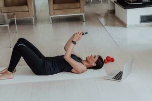 Sportswoman using a smartphone while resting and lying on floor of modern house photo