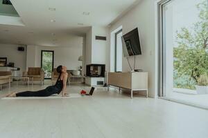 Young Beautiful Female Exercising, Stretching and Practising Yoga with Trainer via Video Call Conference in Bright Sunny House. Healthy Lifestyle, Wellbeing and Mindfulness Concept. photo