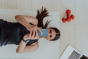 Sportswoman using a smartphone while resting and lying on floor of modern house photo