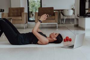 Sportswoman using a smartphone while resting and lying on floor of modern house photo