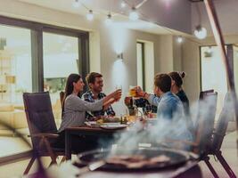 un grupo de joven diverso personas teniendo cena en el terraza de un moderno casa en el noche. divertido para amigos y familia. celebracion de vacaciones, bodas con parilla. foto