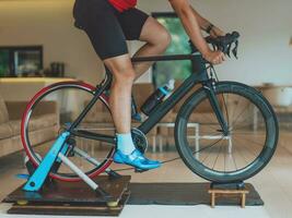 A man riding a triathlon bike on a machine simulation in a modern living room. Training during pandemic conditions. photo