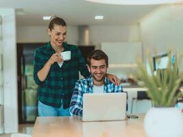 A young married couple is talking to parents, family and friends on a video call via a laptop while sitting in the living room of their modern house photo