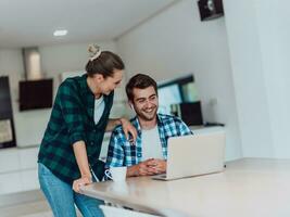 A young married couple is talking to parents, family and friends on a video call via a laptop while sitting in the living room of their modern house photo