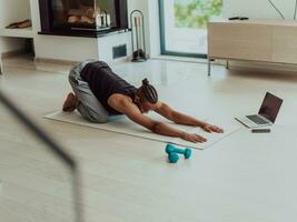 Training At Home. Sporty man doing training while watching online tutorial on laptop, exercising in living room, free space photo