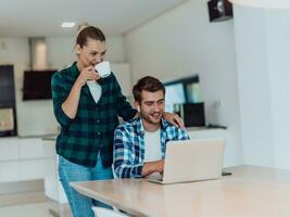 A young married couple is talking to parents, family and friends on a video call via a laptop while sitting in the living room of their modern house photo