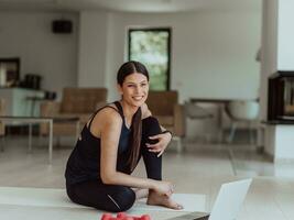 A young woman in sportswear is sitting in the living room and preparing for online training while using a laptop photo