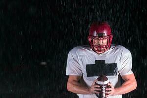 American Football Field Lonely Athlete Warrior Standing on a Field Holds his Helmet and Ready to Play. Player Preparing to Run, Attack and Score Touchdown. Rainy Night with Dramatic Fog, Blue Light photo