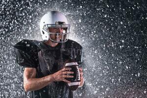 American Football Field Lonely Athlete Warrior Standing on a Field Holds his Helmet and Ready to Play. Player Preparing to Run, Attack and Score Touchdown. Rainy Night with Dramatic Fog, Blue Light photo