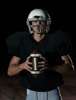 American Football Field Lonely Athlete Warrior Standing on a Field Holds his Helmet and Ready to Play. Player Preparing to Run, Attack and Score Touchdown. Rainy Night with Dramatic Fog, Blue Light photo