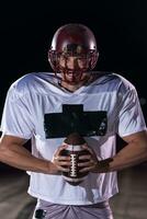 American Football Field Lonely Athlete Warrior Standing on a Field Holds his Helmet and Ready to Play. Player Preparing to Run, Attack and Score Touchdown. Rainy Night with Dramatic Fog, Blue Light photo